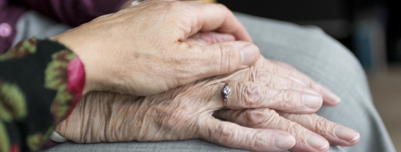 Person placing their hand on top of the hand of an older adult.